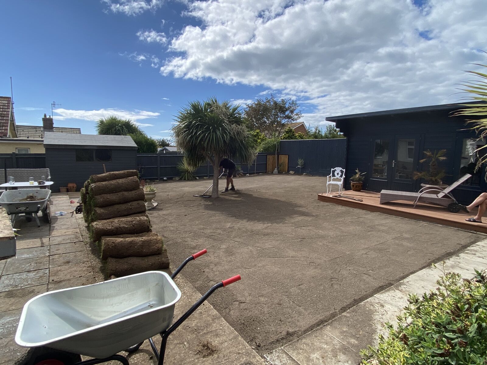 Back garden cleared and levelled ready for turf, with fresh rolls of turf stacked on the patio