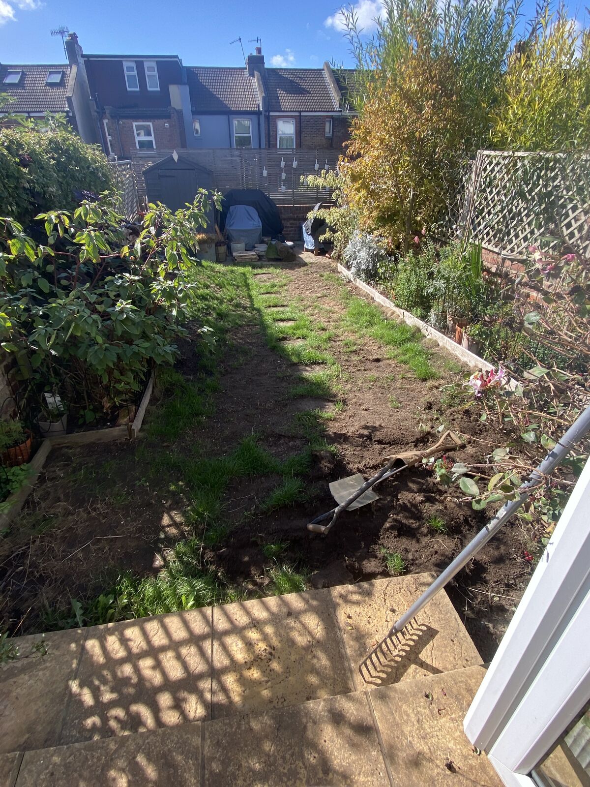 Long terraced back garden with worn grass being dug out ready for preparation