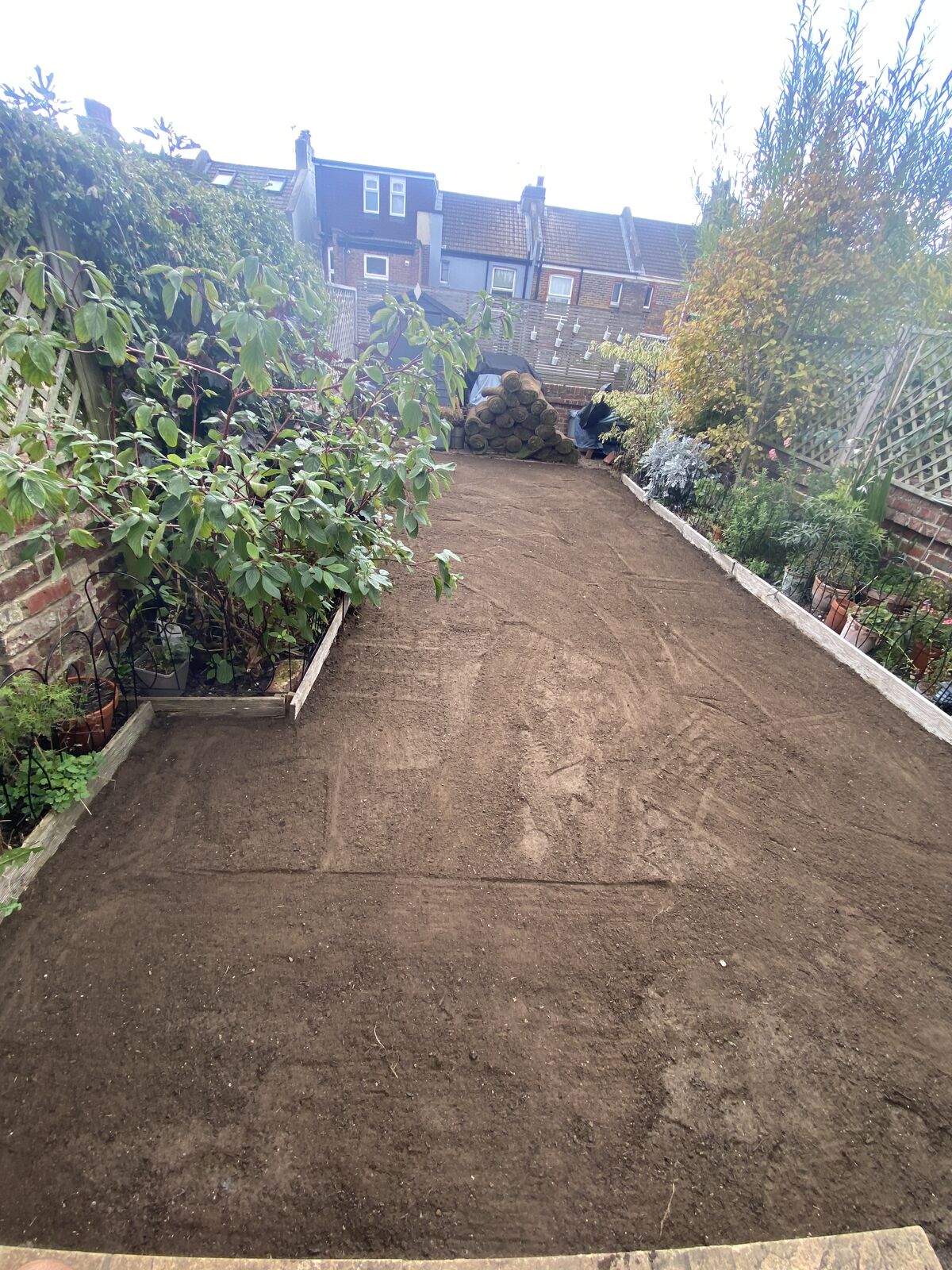 The same terraced garden levelled to bare soil with rolls of turf waiting at the far end
