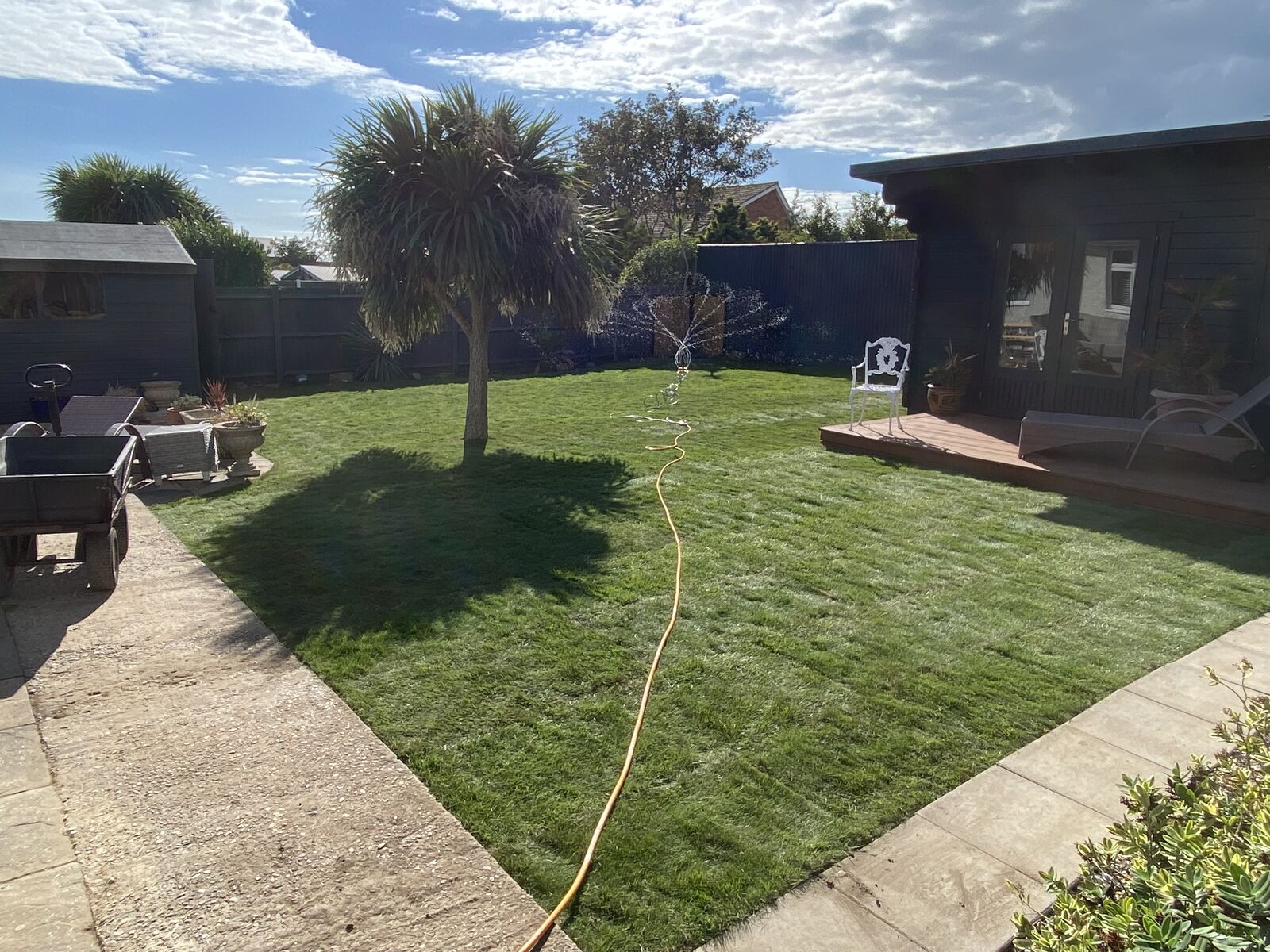 The same back garden finished with a new green lawn being watered by a sprinkler